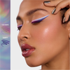 Eine Frau trägt einen auffälligen lilafarbenen und weißen geflügelten Eyeliner, der mit Danessa Myricks Beauty Infinite Chrome Pencil aufgetragen wurde, kombiniert mit glänzenden Lippen und metallischen Nägeln. Farbmuster sind auf der linken Seite zu sehen.