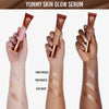 Drei Hände mit unterschiedlichen Hauttönen halten Yummy Skin Glow Serum Tuben und zeigen jeweils drei Muster der Seren auf ihrem Arm.