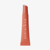 Eine korallenrote Juicy Lip Balm Tube von Dominique Cosmetics mit weißem Text auf weißem Hintergrund.