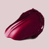 Ein Strich Pillow Soft Hydrating Lip & Cheek Stain in glänzendem Dunkelbeer auf hellbeigem Hintergrund.