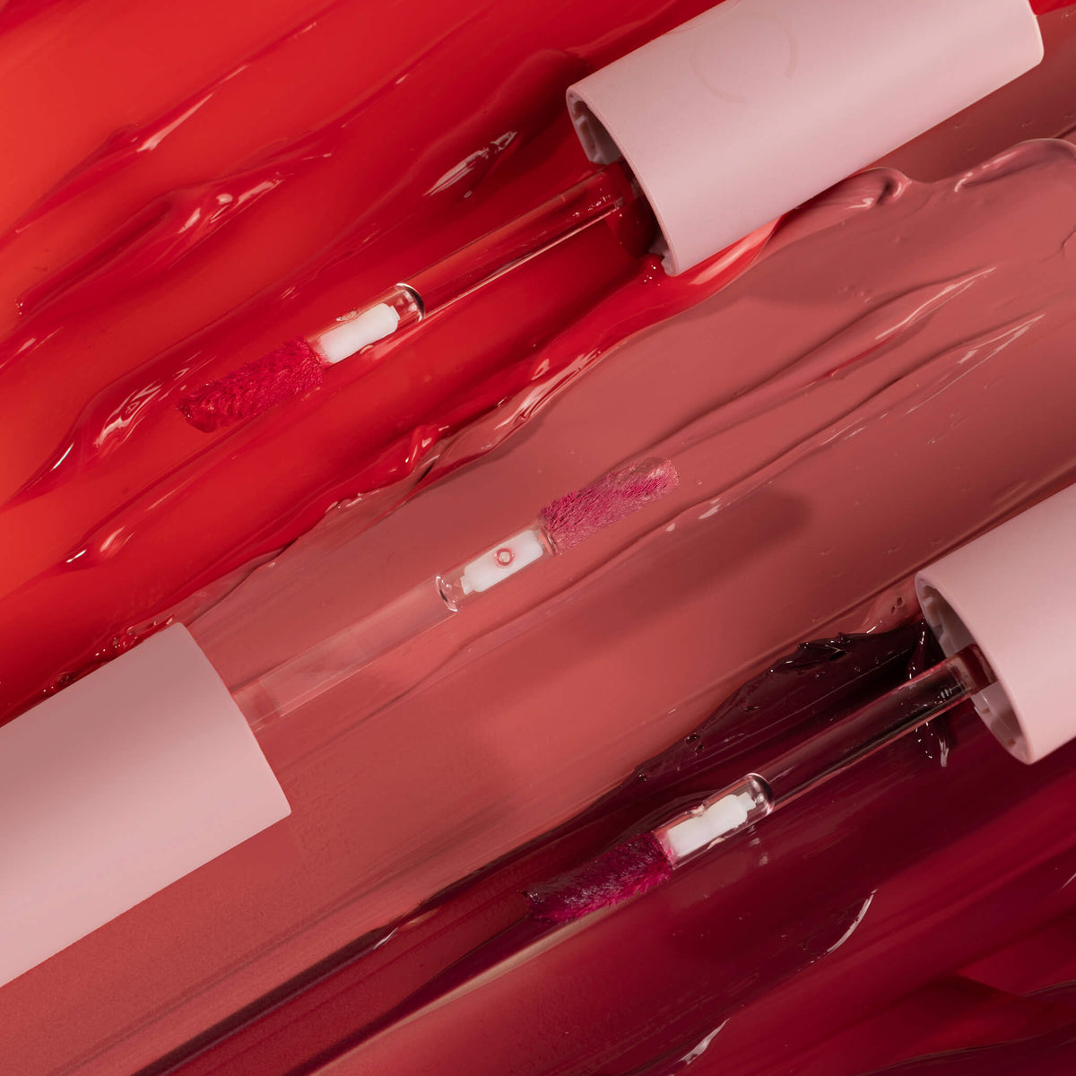 Zwei Pillow Soft Hydrating Lip & Cheek Stain-Applikatoren in Rosa- und Rottönen auf einem glänzenden, marmorierten roten und rosa Hintergrund.