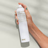 Eine Hand hält eine Sprühflasche Builders Paradise Working Spray vor einem salbeigrünem Hintergrund.