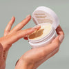 Eine Hand schöpft Crop Strutters Construction Cream aus einem offenen weißen Tiegel .