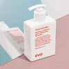 Weiße Pumpflasche Ritual Salvation Repairing Conditioner steht auf einer rosa Oberfläche neben einem Spiegel, umgeben von Wassertropfen.