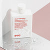 Eine weiße Flasche Ritual Salvation Repairing Shampoo steht auf einer reflektierenden Oberfläche mit Wassertropfen.