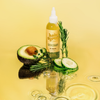 Growsmary Haaröl von Hair Syrup mit Avocado, Gurkenscheiben und Rosmarinzweigen auf einem leuchtend gelben Hintergrund mit Wasserkräuseln.