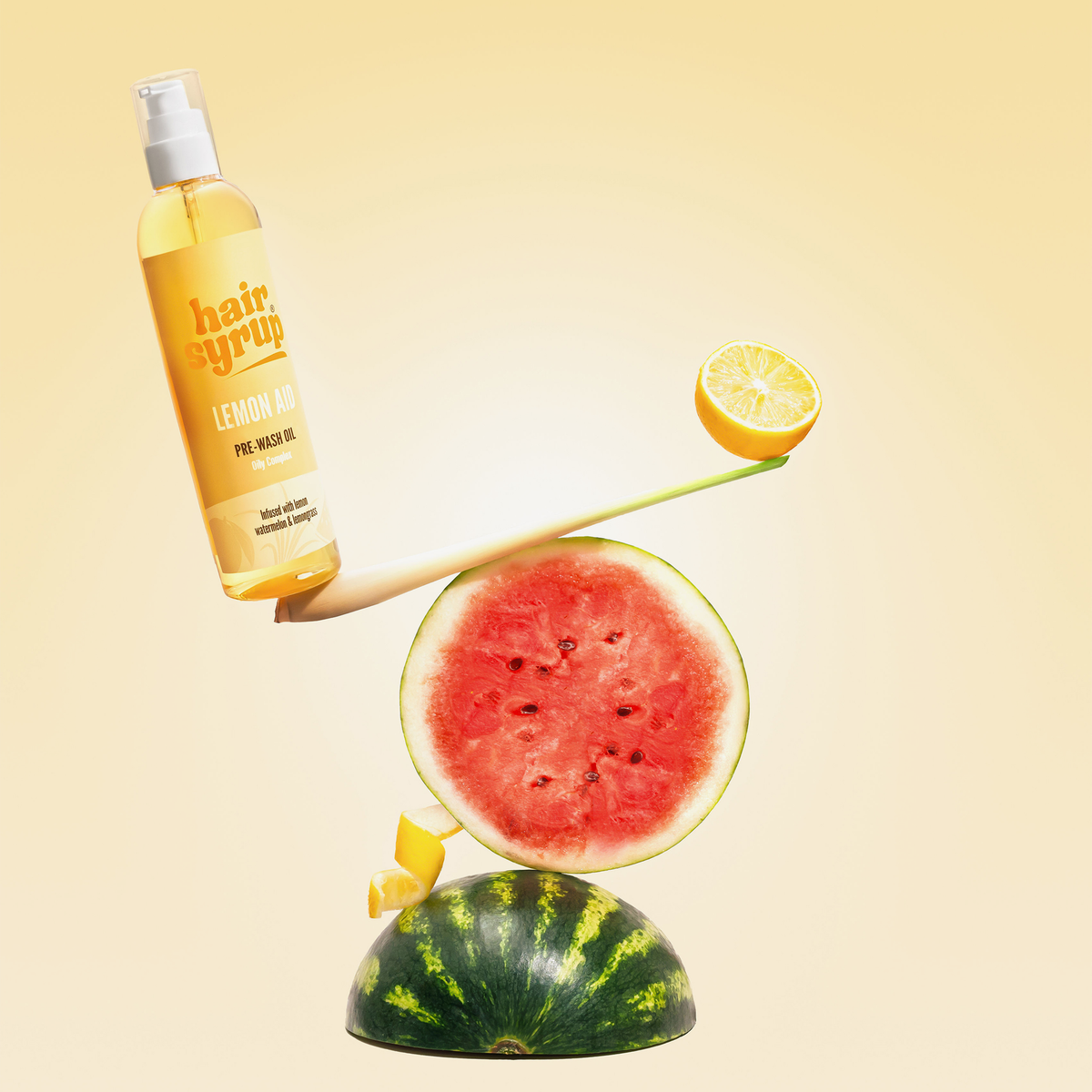 Eine Flasche Hair Syrup Lemon-Aid balanciert mit einer Zitronenscheibe auf einer Wippe auf einer Wassermelone.