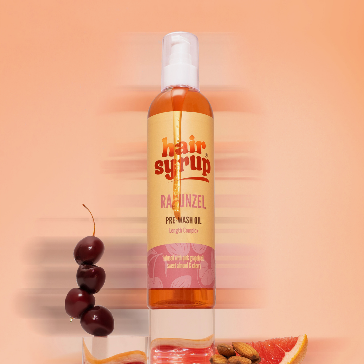 Eine Flasche Haarsirup Rapunzel Haaröl mit Kirschen, Mandeln und einer Grapefruitscheibe daneben.