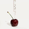 Eine Pipette verteilt die Flüssigkeit Very Cherry von Hair Syrup auf eine glänzende Kirsche mit langem Stiel vor weißem Hintergrund.