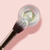 Der K10: Highlighter Brush liegt auf einem geöffneten Tiegel Shadow Potion auf rosa Hintergrund.