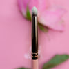 Der K24: Smoky Pencil, ein Make-up-Pinsel mit goldener Zwinge aufrecht vor einem rosa Hintergrund mit verschwommener Blume.