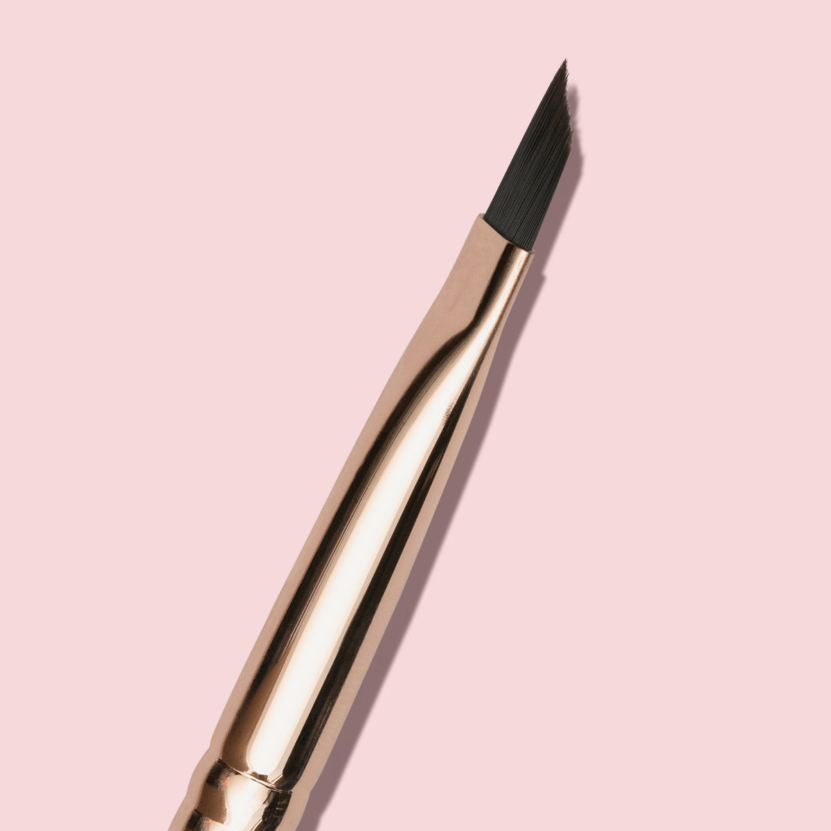 Eine Nahaufnahme des K26: Eyeliner Brush, eines abgewinkelten Make-up-Pinsels abgebildet auf einem hellrosa Hintergrund.