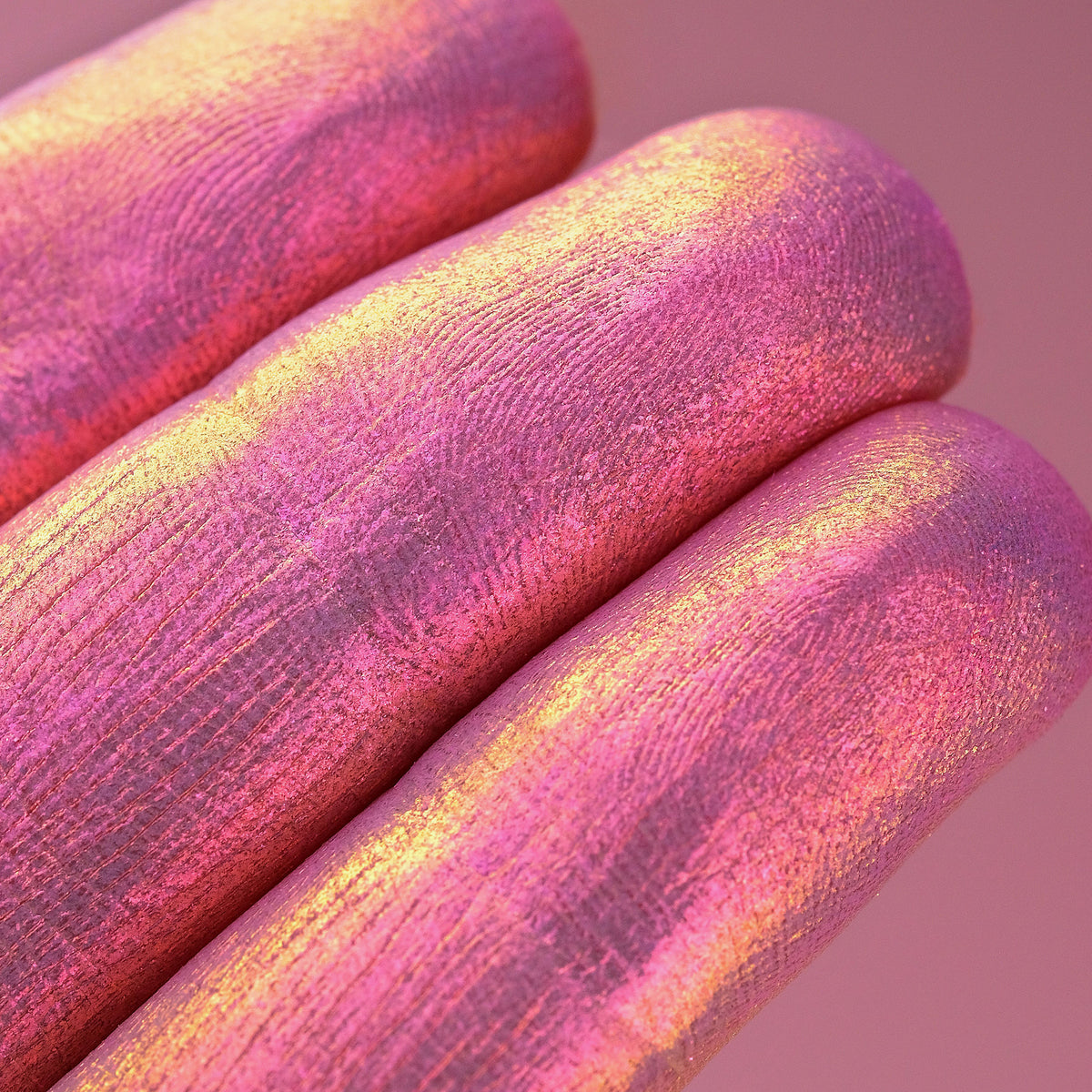 Nahaufnahme von Fingerspitzen, die in den Opal Moonstone Loose Multichrome Eyeshadow Cutie Pie getaucht wurde und gold-rosa glitzert.