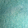 Nahaufnahme der Textur des Pastel Duochromes Loose Eyeshadow Buttons; ein türkis-grün schimmerndes Pigment.