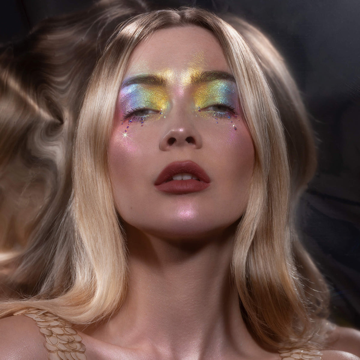 Eine Frau mit blondem Haar in bunt glitzerndem Augenmakeup, geschminkt mit dem Pastel Duochromes Loose Eyeshadow.