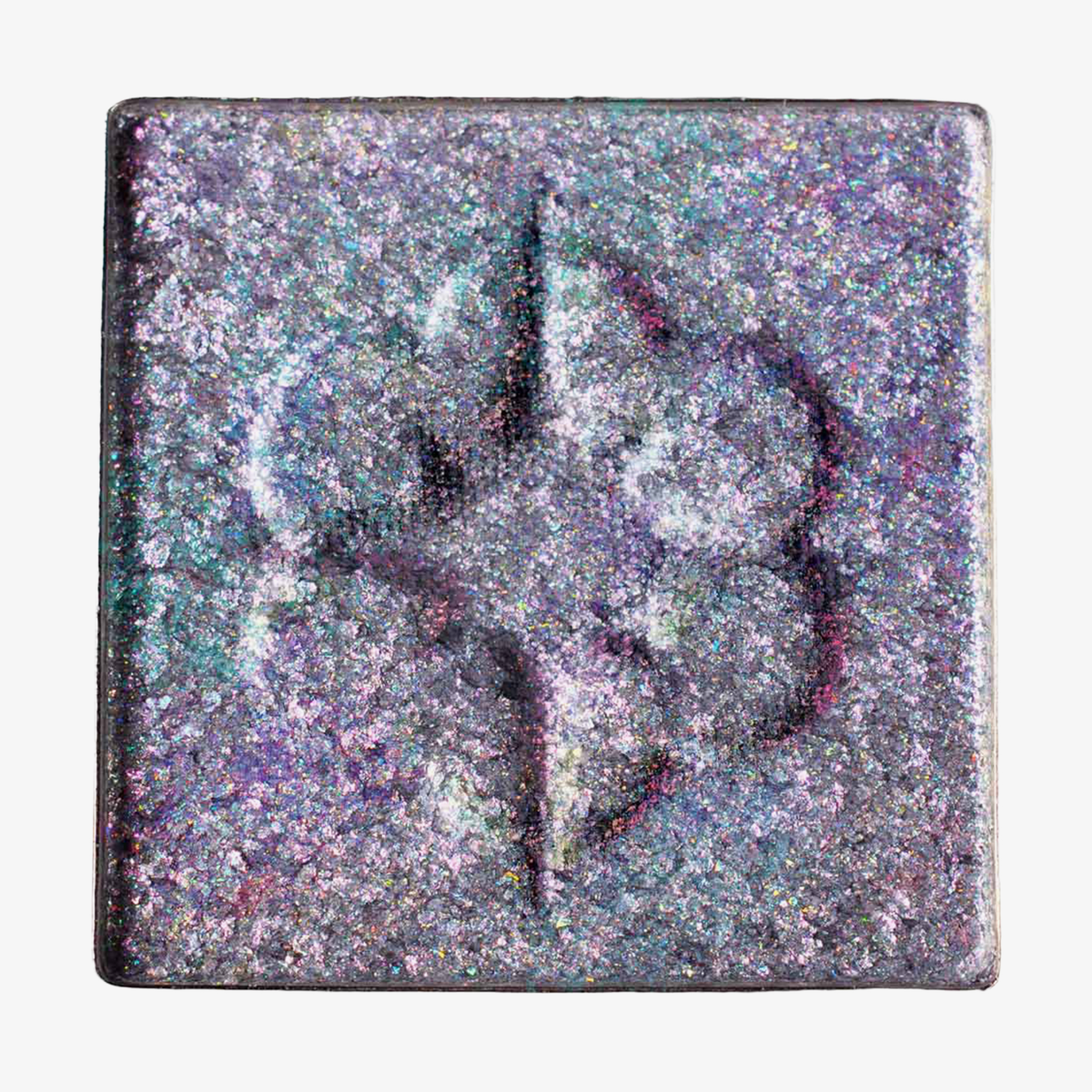 Quadratisches Pfännchen des MAGNETIC™ Pressed Multichrome Shadow "Moonstone" von Lethal Cosmetics in glitzerndem lila-blaugrün mit floraler Prägung in der Mitte.