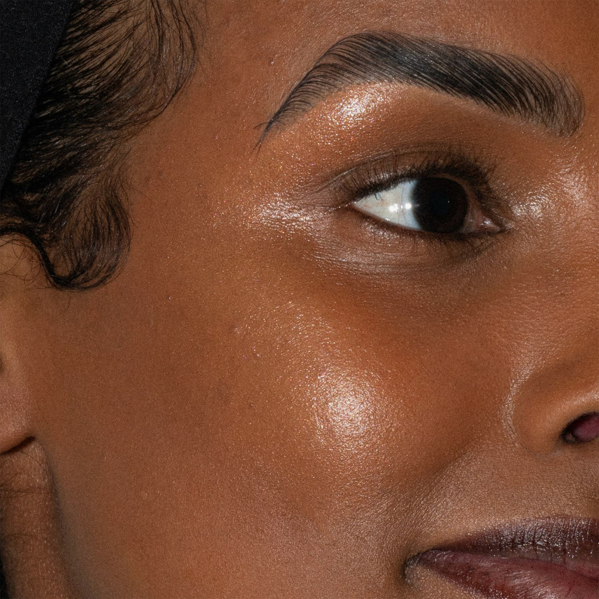 Nahaufnahme eines Gesichts mit einem Auge, einer Augenbraue und leuchtender Haut, hervorgehoben durch LH Cosmetics Artistick Highlighter.