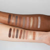 Auf zwei Unterarmen unterschiedlicher Hautfarbe werden Swatches der Boring Nude Palette von LH Cosmetics mit neutralen und metallischen Lidschattentönen gezeigt.