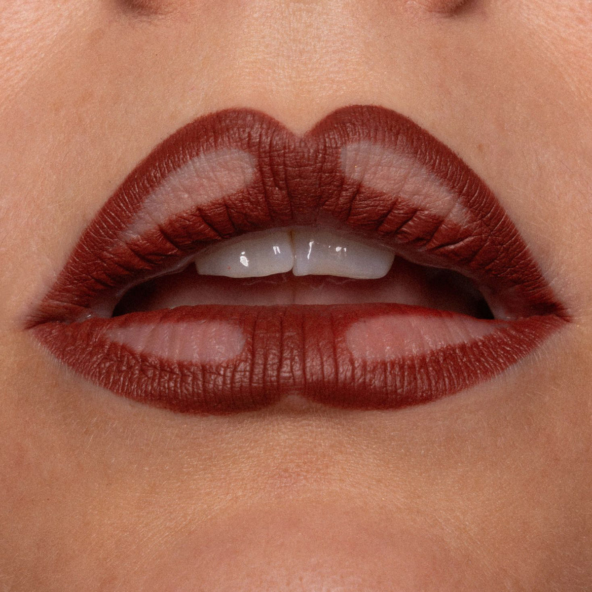 Nahaufnahme geschminkter Lippen mit braunem Lippenstift und bewusst ausgesparten Stellen, die ein verspieltes, grafisches Muster ergeben.