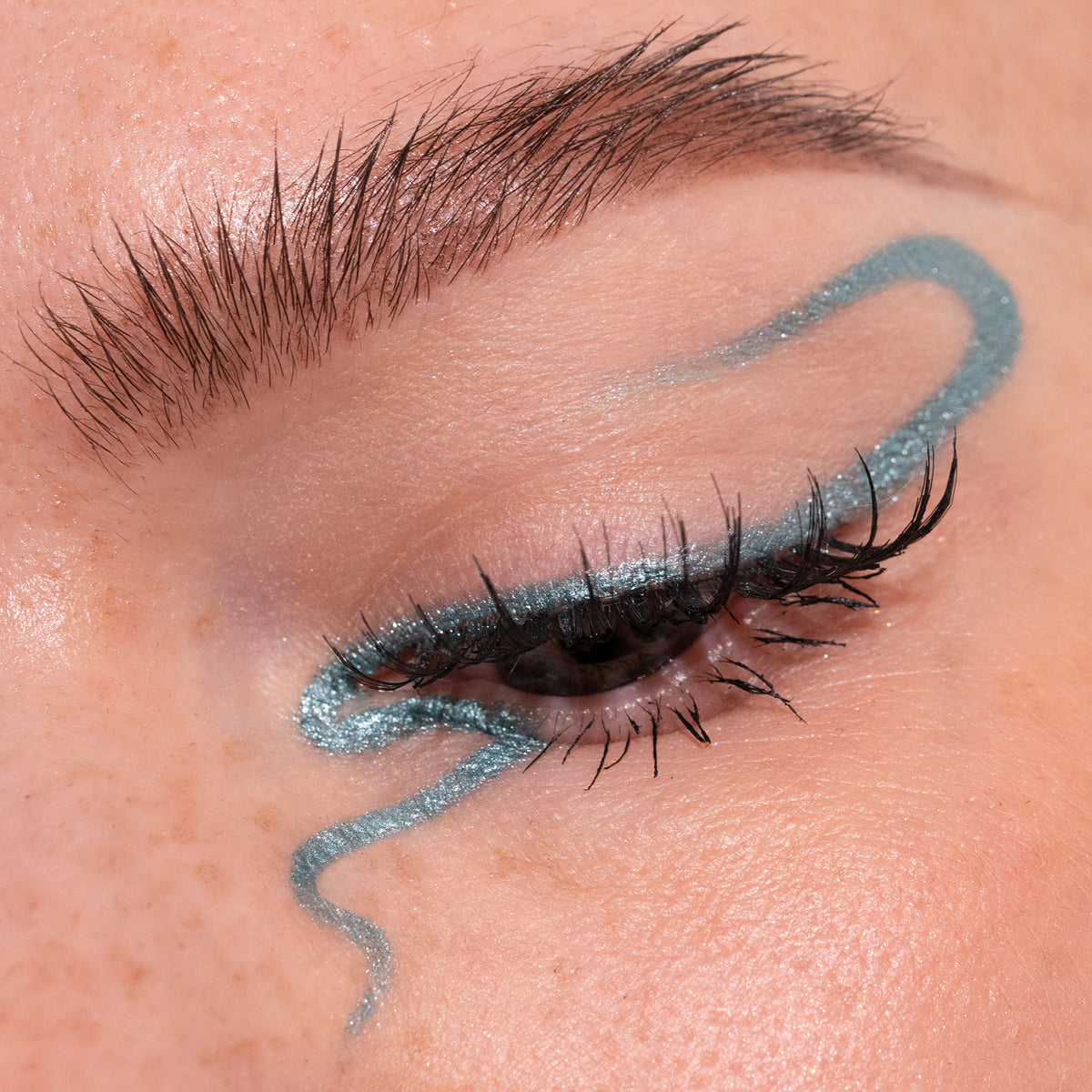 Nahaufnahme eines Auges zeigt einen kreativen türkis glitzernden Eyeliner, der mit dem Crayon Risha von LH Cosmetics kreiert wurde.
