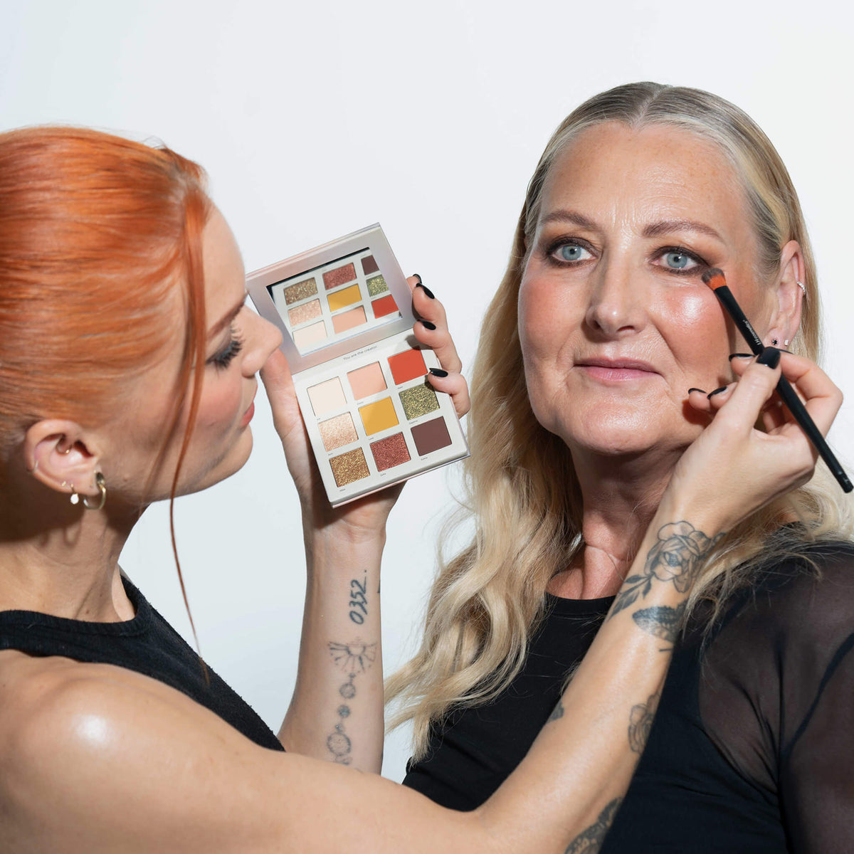 Eine junge Frau verwendet die LH Cosmetics Creator Palette und einen Make-up-Pinsel, um einer älteren Frau Lidschatten aufzutragen.