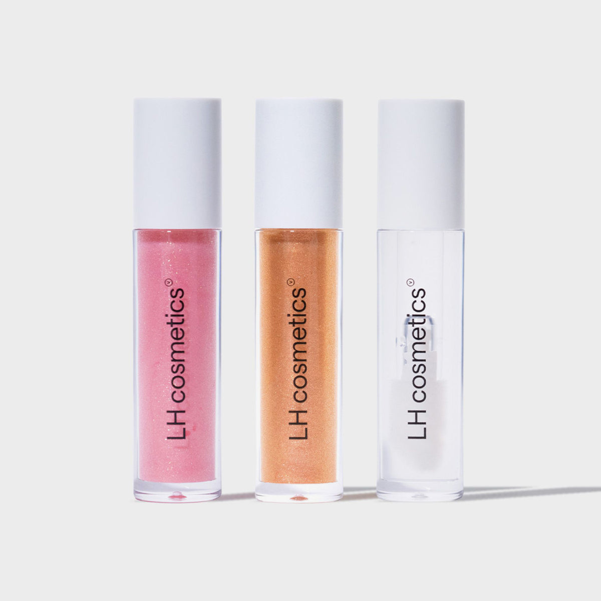 Drei Lipgloss-Tuben des LH Cosmetics Glazed in den Farbtönen Pink, Orange und Klar vor weißem Hintergrund.