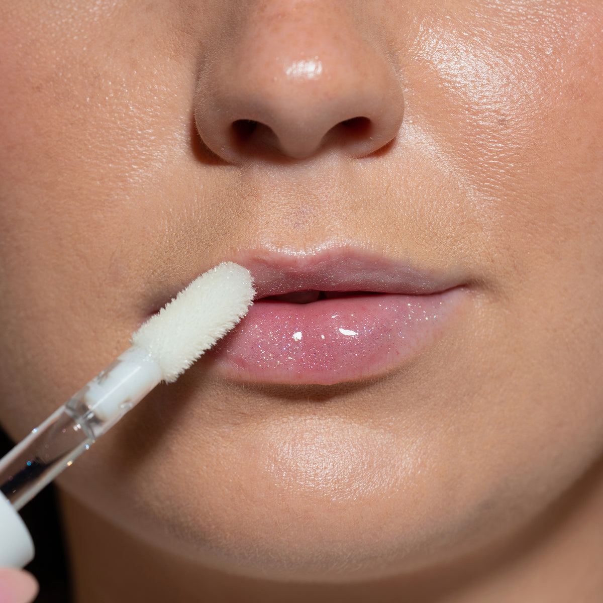 Nahaufnahme von Lippen einer Person mit hellem Teint mit transparent glitzerndem Glazed Yum Lipgloss von LH Cosmetics.