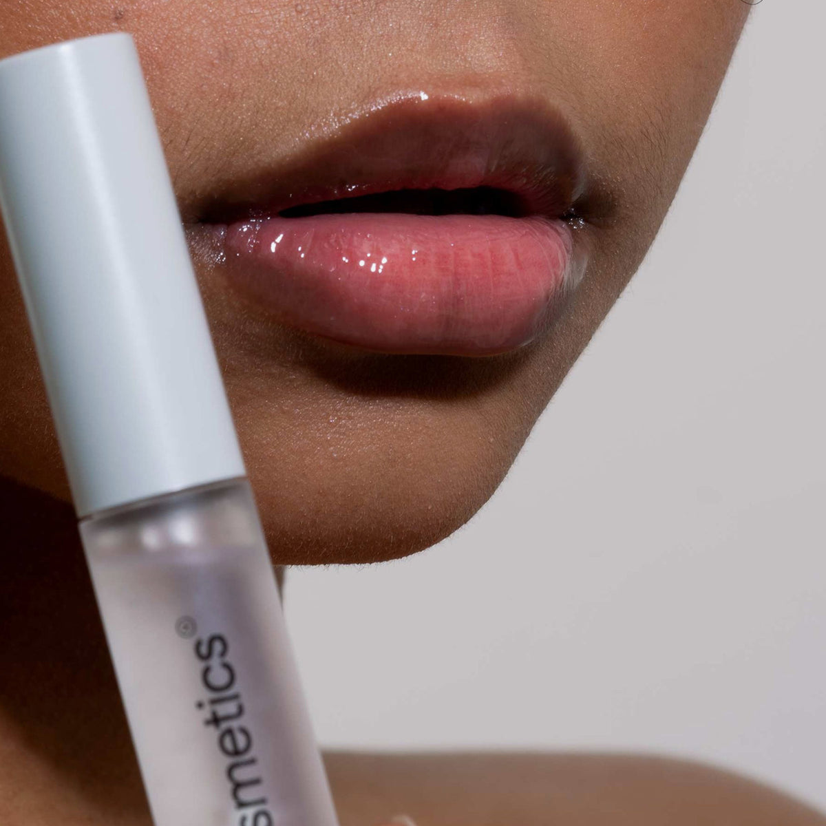 Nahaufnahme von glänzenden Lippen und einer Person, die Gloil von LH Cosmetics hält.