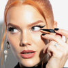 Eine Frau mit rotem Haar trägt Infinity Ink Eyeliner von LH Cosmetics auf und kreiert einen auffälligen Eyeliner-Look.