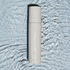 Eine Flasche LH Cosmetics On Set – Subtle Glow Setting Spray steht auf plätscherndem, reflektierendem Wasser.