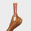 Eine Hand hält eine roséfarbene Tube LH Cosmetics Shaping Light Rose Glow vor schlichtem weißen Hintergrund.