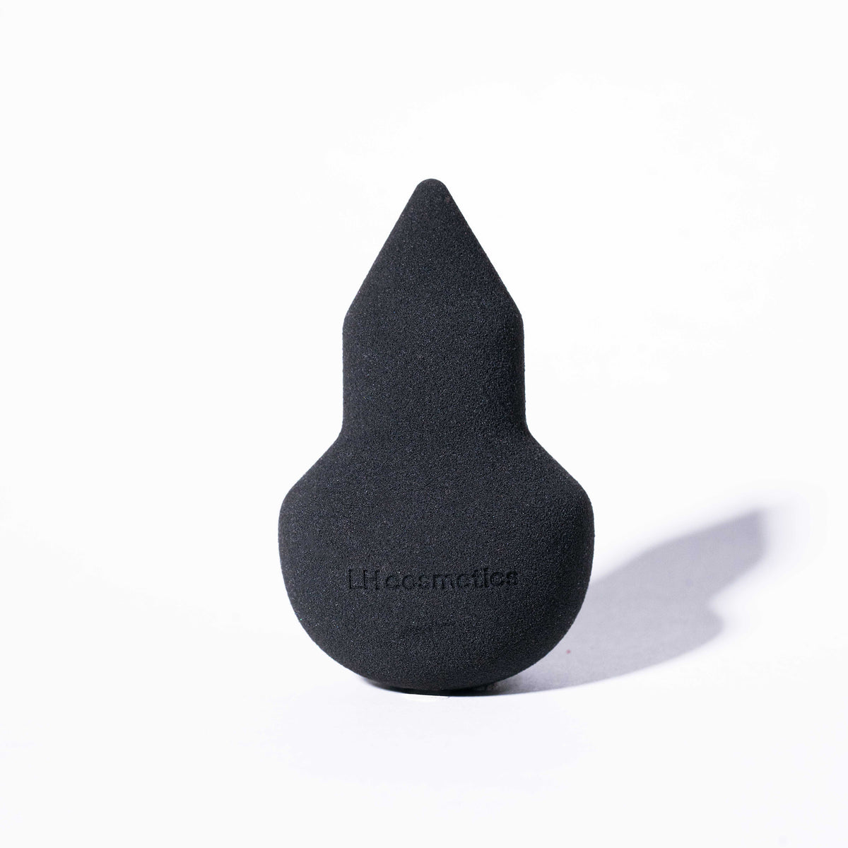 Schwarzer Make-up-Schwamm "The Sponge" mit spitzer Spitze und runder Basis, steht aufrecht vor weißem Hintergrund, Logo LH Cosmetics sichtbar.