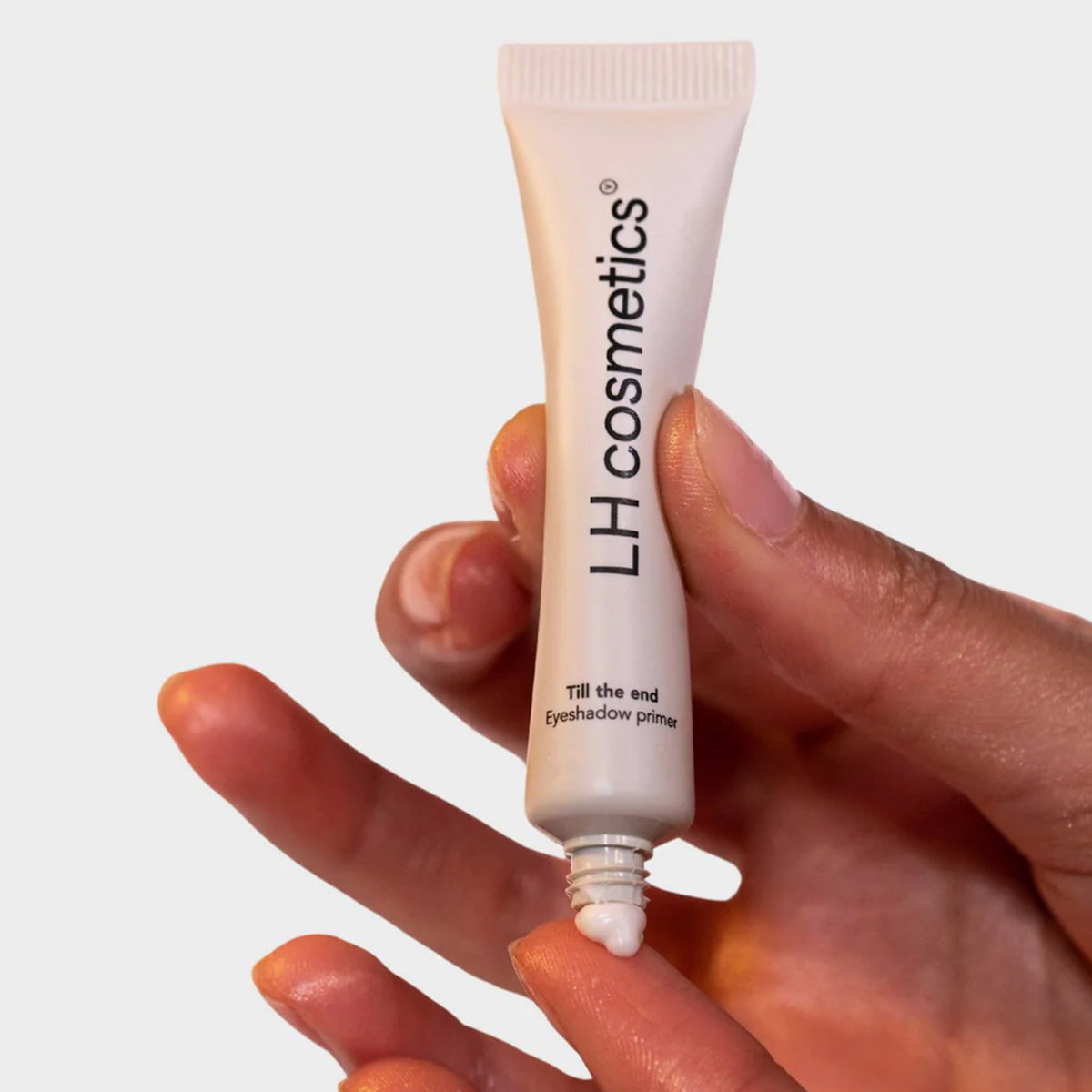 Eine Hand drückt den LH Cosmetics Till The End Eyeshadow Primer auf eine Fingerspitze vor einem neutralen Hintergrund.