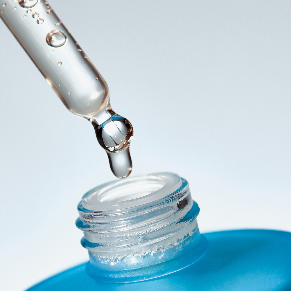 Eine Pipette gibt Scalp Care Density Serum in den Hals einer offenen blauen Flasche.