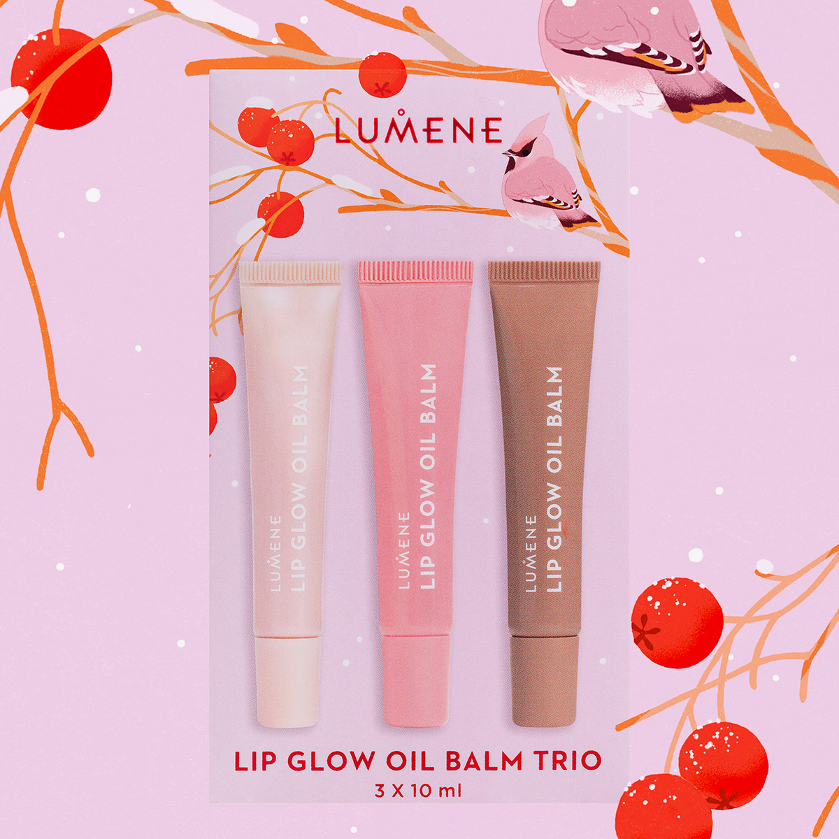 Das Lumene Lip Glow Oil Balm Set 2025 enthält drei Farbtöne - Rosa, Pfirsich und Beige - vor einem dekorativen Hintergrund aus Vögeln und Zweigen.
