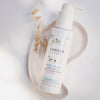 Weiße Pumpflasche Lumene NORDIC HYDRA [LAHDE] Oat Milk Oil Cleanser liegt auf einer organisch-geformten weißen Schale mit getrockneten Haferstängeln daneben.