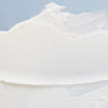 Weiße Creme-Textur der NORDIC SENSITIVE [HERKKÄ] Rich Day Cream auf einem hellblauen Hintergrund verteilt.