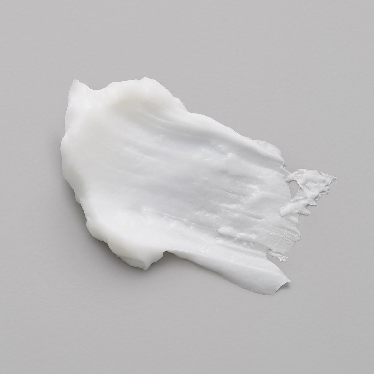 Weißer Klecks der maria nila Pure Volume Masque auf einer hellgraue Oberfläche.