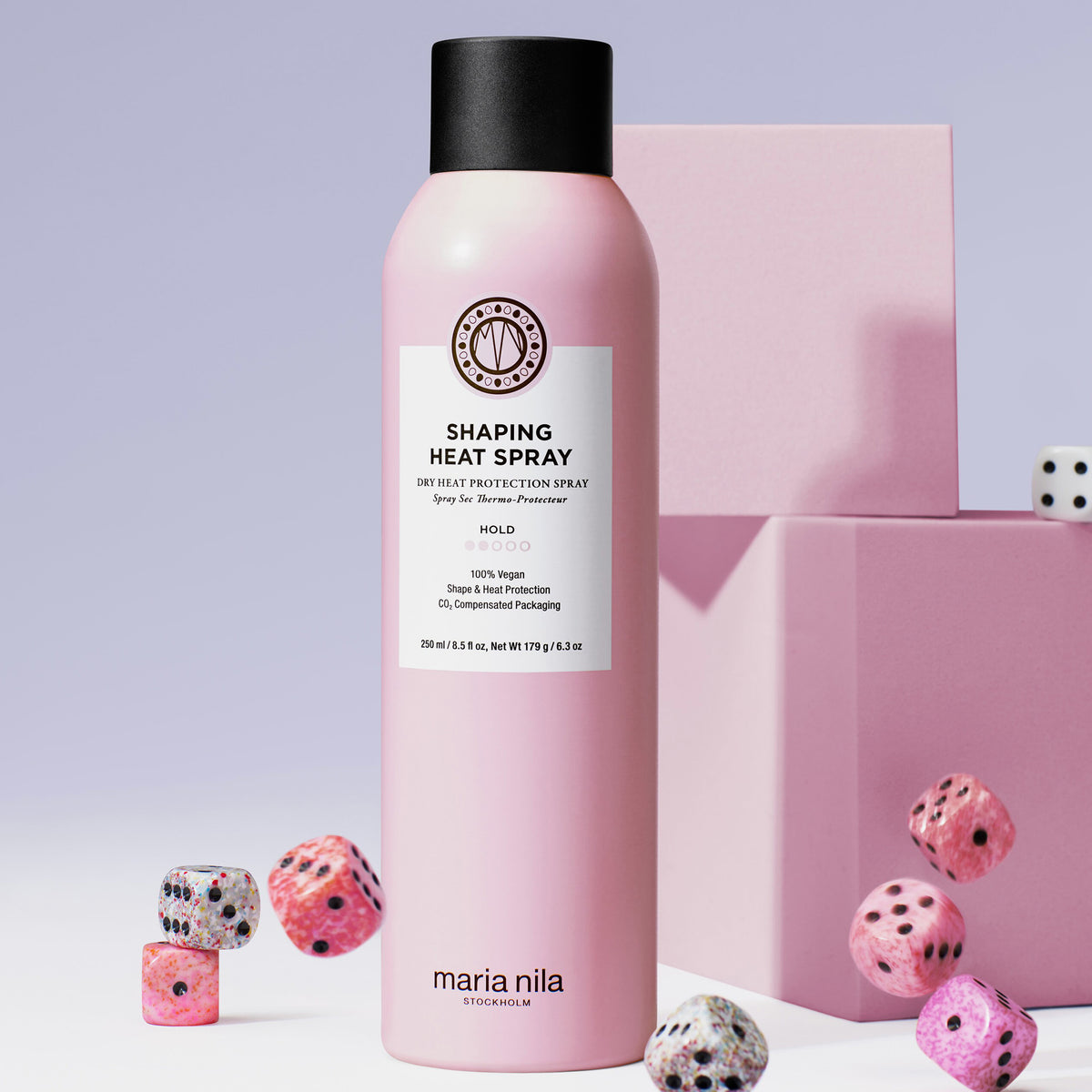 Eine Flasche maria nila Shaping Heat Spray ist umgeben von rosa Würfeln auf einem passenden rosa Hintergrund.