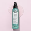 Eine Flasche maria nila True Soft Argan Oil mit darunter verschüttetem Öl liegt auf einem hellrosa Hintergrund.