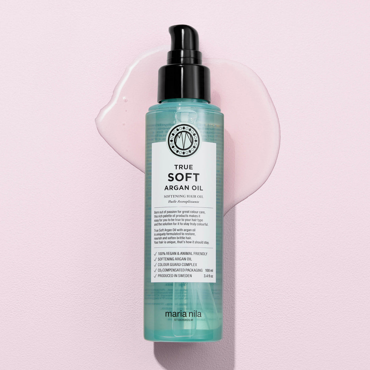 Eine Flasche maria nila True Soft Argan Oil mit darunter verschüttetem Öl liegt auf einem hellrosa Hintergrund.