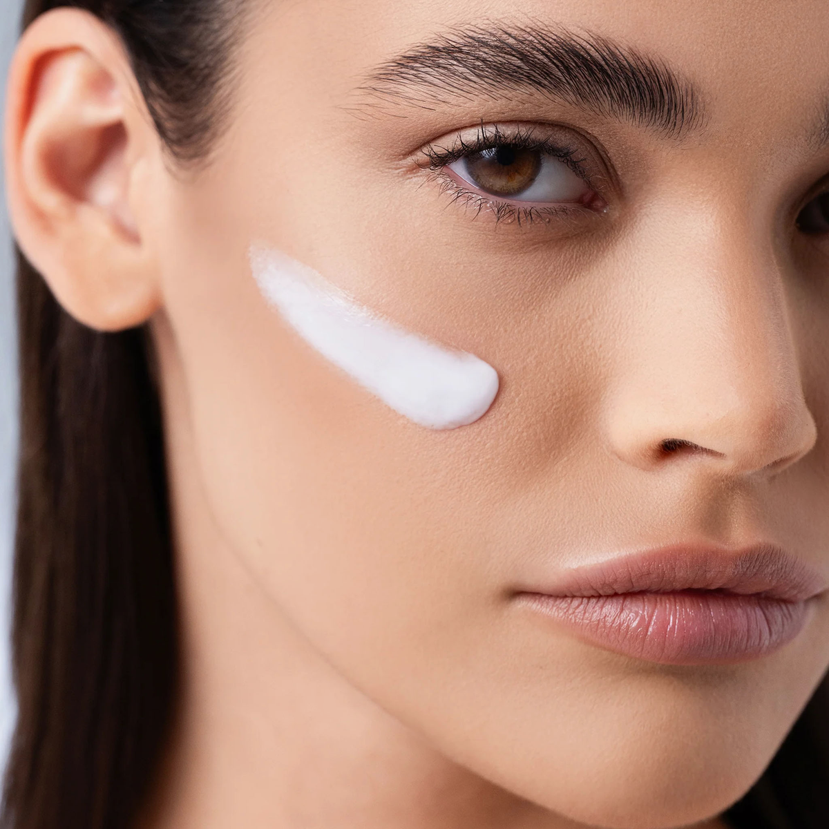 Nahaufnahme eines Frauengesichts mit glatter Haut und natürlichem Make-up, das den Chrono Flawless Primer von Mesauda Beauty als weißen Streifen auf der Wange zeigt.