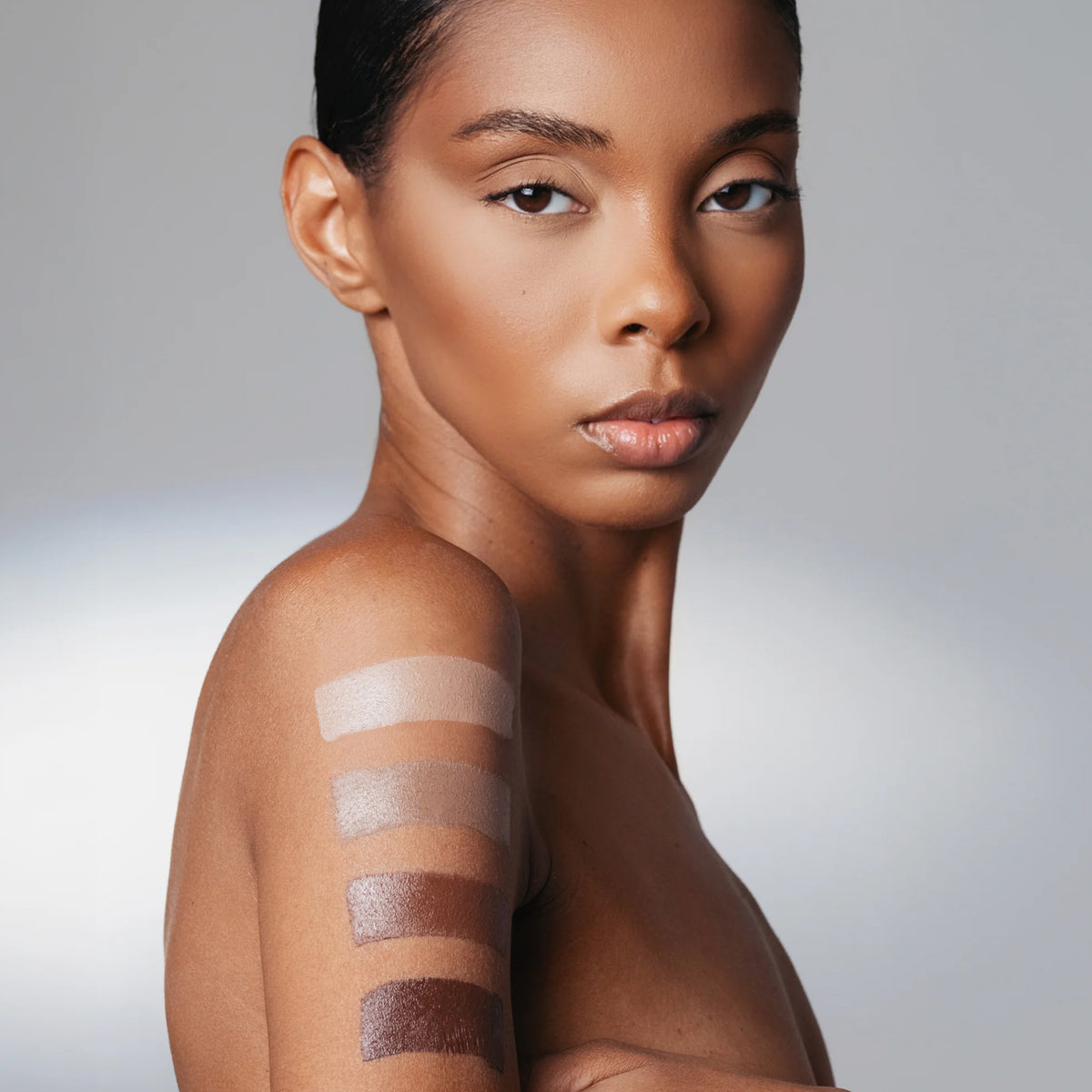 Frau mit makellosem dunklem Teint, auf deren Oberarm vier Swatches des The Mood Contrast in verschiedenen Brauntönen aufgetragen sind.