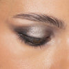 Ein geschlossenes Auge mit silbernem und schwarzem Smokey-Eyeshadow, definierten Brauen und glatter, strahlender Haut, kreiert mit Bare Harmony 2.0 von Mesauda Beauty.