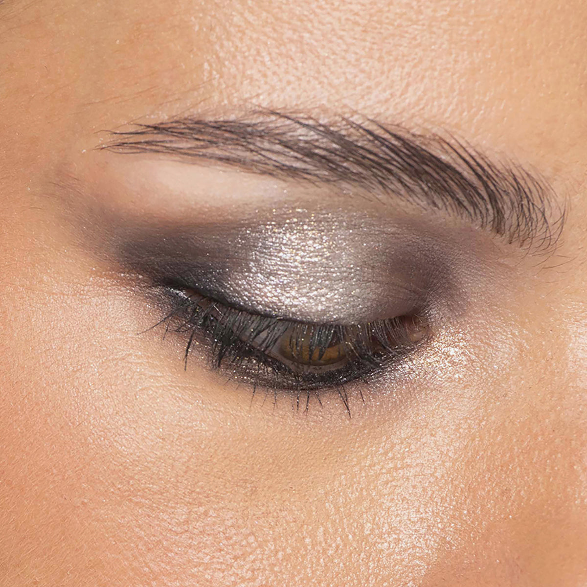 Ein geschlossenes Auge mit silbernem und schwarzem Smokey-Eyeshadow, definierten Brauen und glatter, strahlender Haut, kreiert mit Bare Harmony 2.0 von Mesauda Beauty.