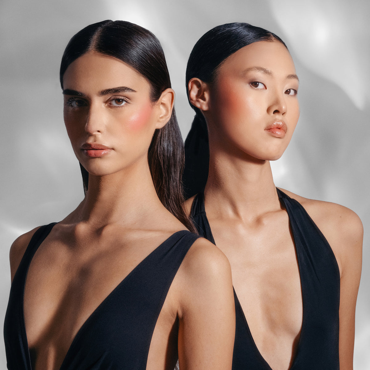 Zwei dunkelhaarige Models mit dem „Flush of Blush“ auf den Wangen, posieren mit vor einem hellen Hintergrund.