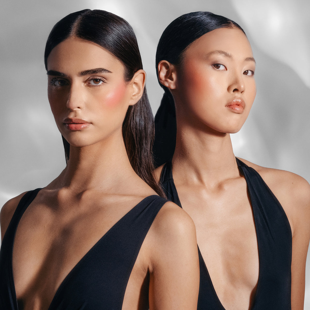Zwei Models mit dem Flush of Light auf den Wangen in schwarzen Outfits vor einem hellem Hintergrund.