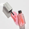 Eine Flasche Mesauda Beauty LIPOILOGY™ Lipgloss mit verschüttetem rosafarbenem Gloss und einem Applikator.