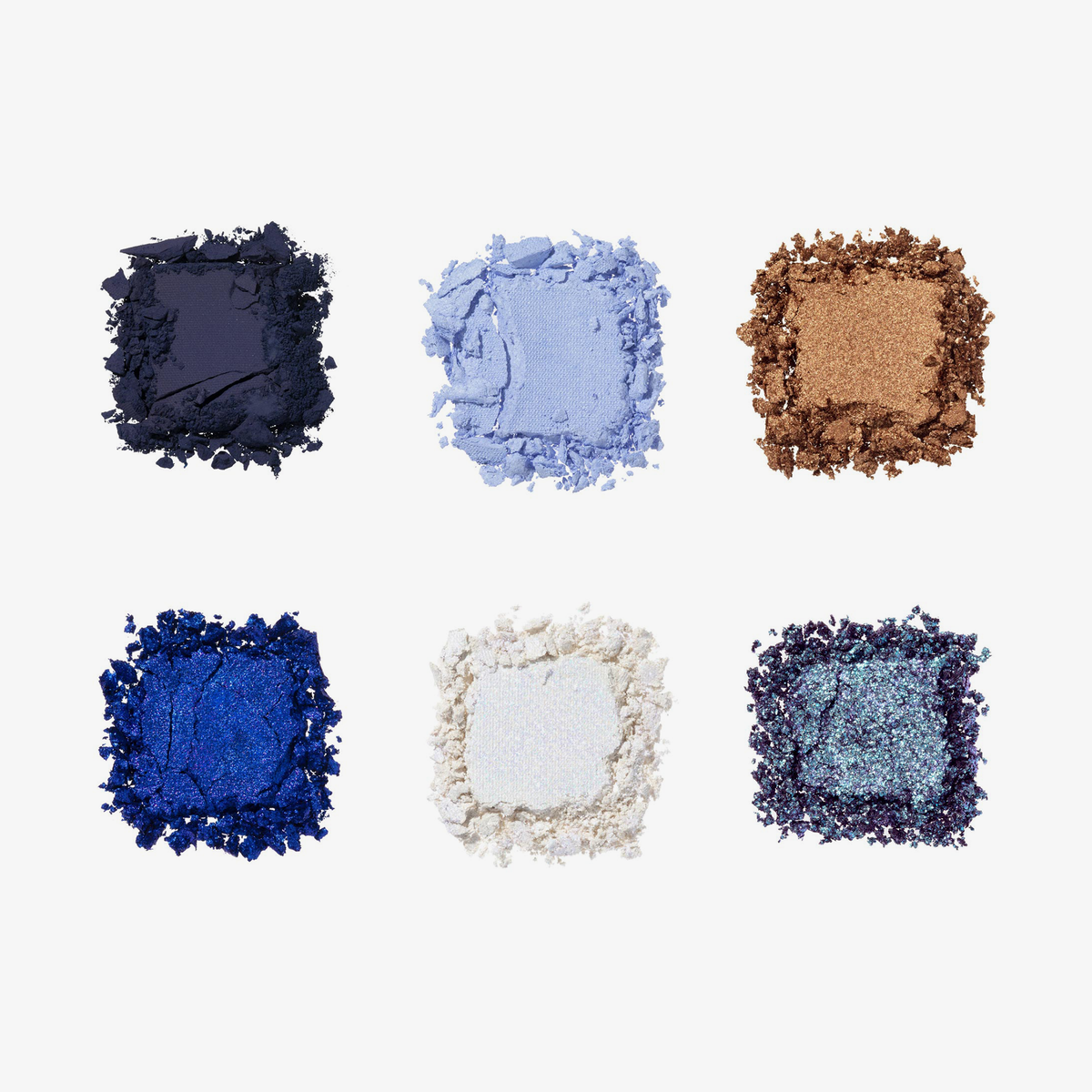 Sechs zerkleinerte Lidschatten der Cutie Palette in Marineblau, Hellblau, Bronze, Königsblau, Weiß und schimmerndem Blaugrün auf weißem Hintergrund.