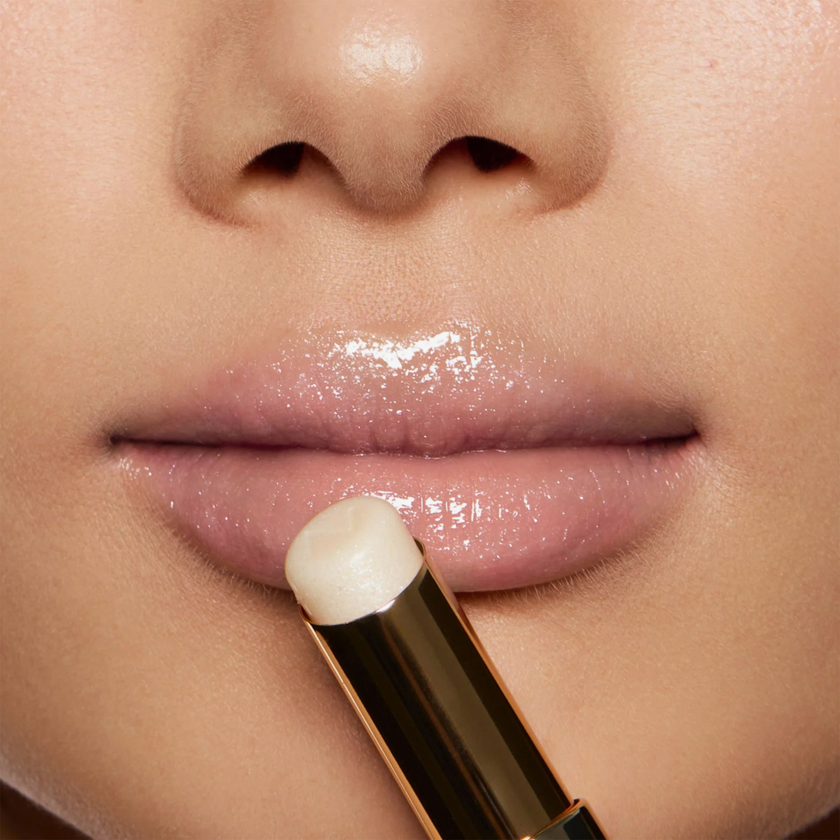 Nahaufnahme von glänzenden Lippen, als eine Person den Beyond Jelly Lipstick Pearlescent von NABLA Cosmetics aus einer goldenen Tube aufträgt.